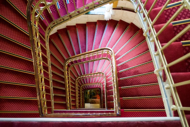 Tiro de ángulo alto de una escalera de caracol rosa con manijas doradas en un hermoso edificio