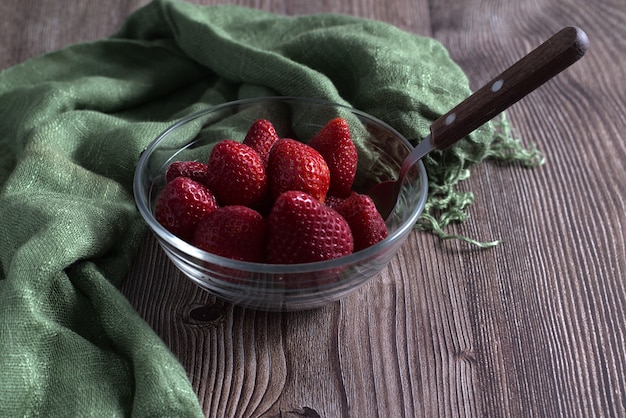 Tiro de ángulo alto de fresas frescas y un textil verde en un recipiente de vidrio sobre una superficie de madera