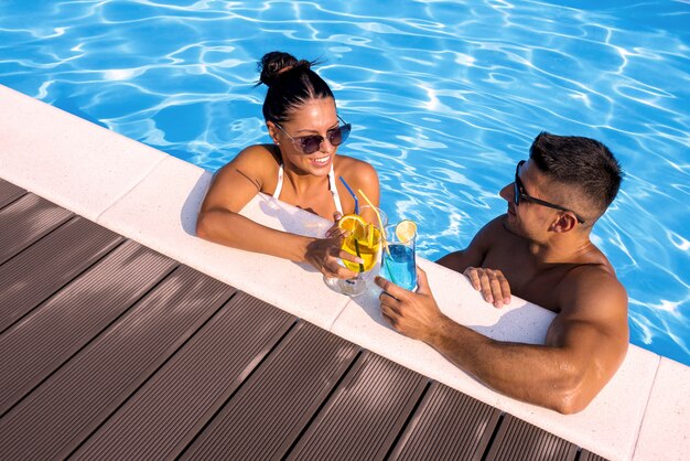 Tiro de ángulo alto de un grupo sonriente de una pareja sosteniendo cócteles en la piscina