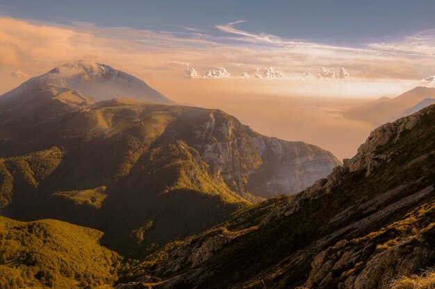 Tiro de ángulo alto de hermosas montañas verdes cubiertas de nubes bajo el cielo colorido