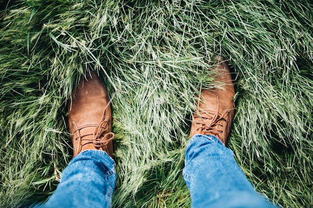 Tiro de ángulo alto de una persona con zapatos de cuero y jeans de pie sobre un campo de hierba