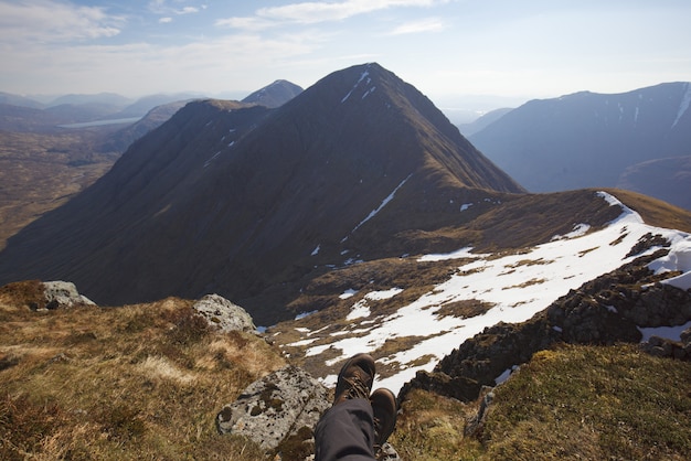 Tiro de ángulo alto de las piernas de un humano sentado en el suelo en la cima de las montañas