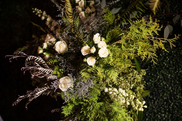 Tiro de ángulo alto de un ramo con hojas perennes y rosas blancas bajo las luces