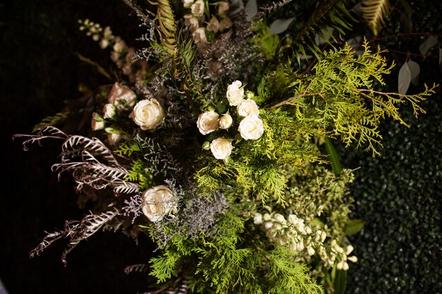 Tiro de ángulo alto de un ramo con hojas perennes y rosas blancas bajo las luces