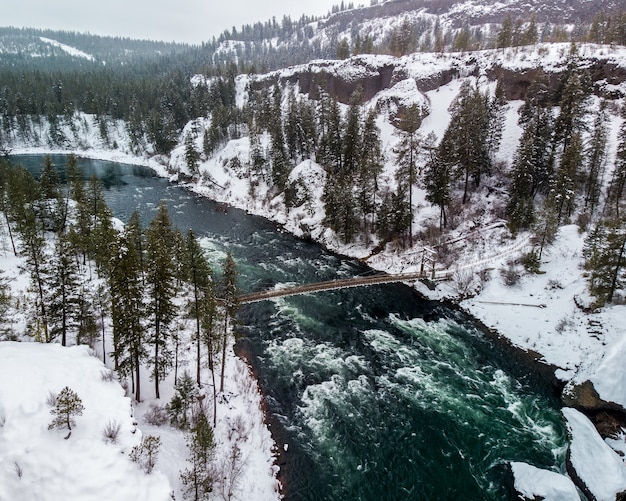 Tiro de ángulo alto de un río en medio de montañas nevadas cubiertas de árboles