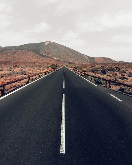 Tiro de ángulo alto vertical de una carretera rodeada de colinas bajo el cielo gris