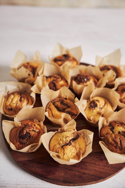 Tiro de ángulo alto vertical de deliciosos muffins de chocolate en una placa de madera sobre una mesa blanca