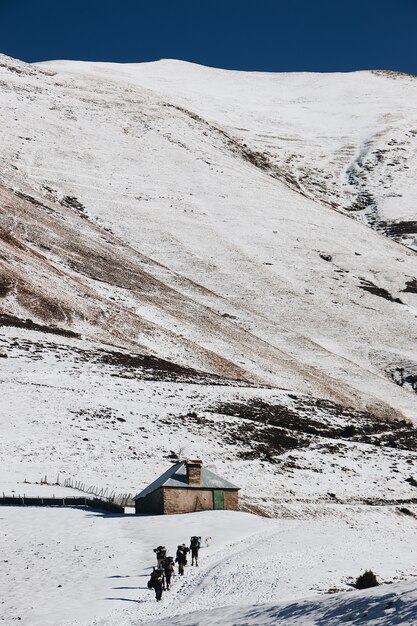 Tiro de ángulo alto vertical de excursionistas acercándose a la pequeña cabaña en las montañas nevadas