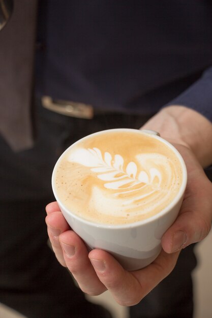 Tiro de ángulo alto vertical de un hombre sosteniendo una taza de capuchino