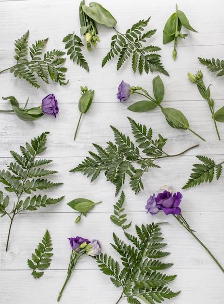 Foto gratuita tiro de ángulo alto vertical de lisianthus púrpura flores y hojas verdes sobre una superficie de madera