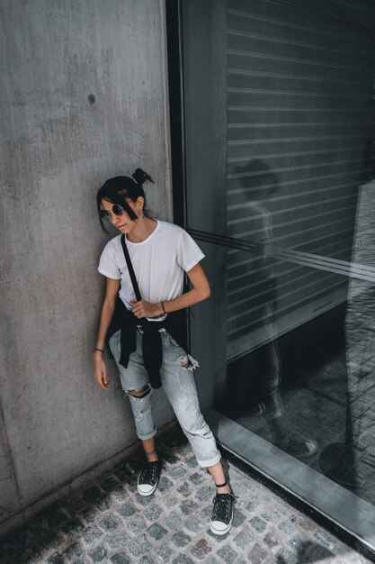 Tiro de ángulo alto vertical de una mujer con estilo hipster con gafas de sol redondas posando en una calle