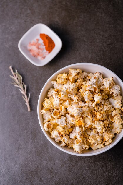 Tiro de ángulo alto vertical de un plato de palomitas de maíz cerca de un pequeño plato de especias sobre una superficie gris