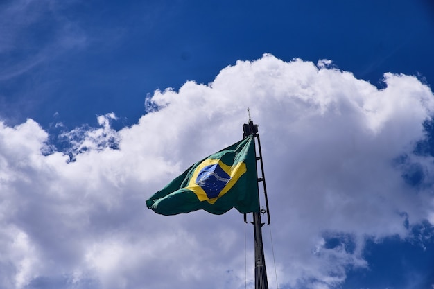 Tiro de ángulo bajo de la bandera de Brasil bajo las hermosas nubes en el cielo azul