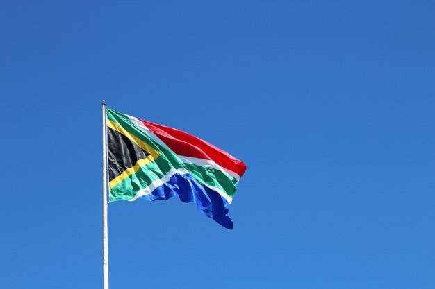 Tiro de ángulo bajo de la bandera de Sudáfrica en el viento bajo el cielo azul claro