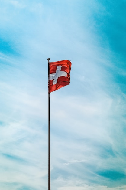 Tiro de ángulo bajo de la bandera de Suiza en un poste bajo el impresionante cielo nublado