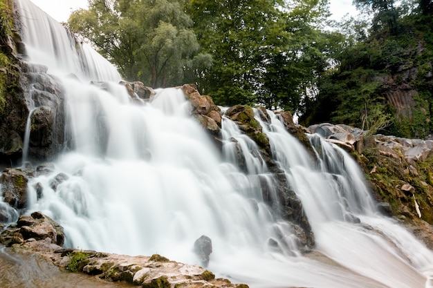 Tiro de ángulo bajo de una cascada rocosa con árboles verdes en el fondo