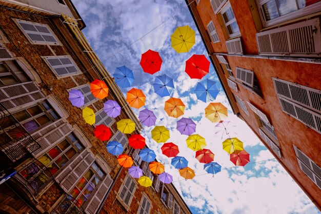 Tiro de ángulo bajo de coloridos paraguas colgando en medio de edificios con cielo nublado