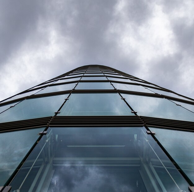 Foto gratuita tiro de ángulo bajo de un edificio de gran altura en una fachada de vidrio bajo las nubes de tormenta