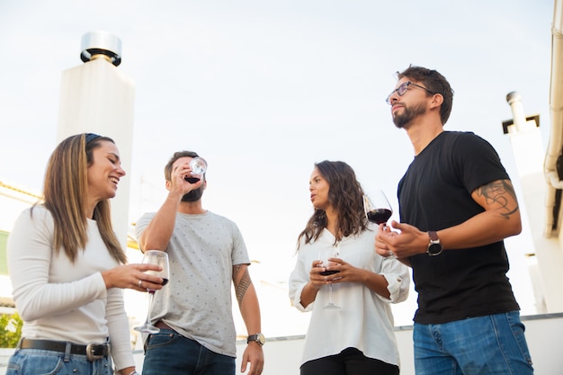 Tiro de ángulo bajo de gente sonriente bebiendo vino tinto y hablando