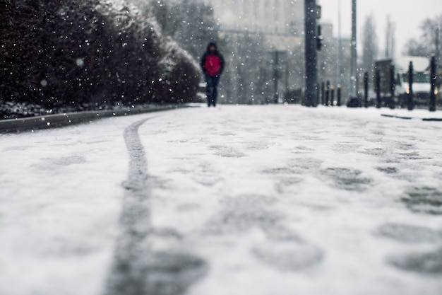 Tiro de ángulo bajo de una persona que camina sobre la acera cubierta de nieve bajo la nieve