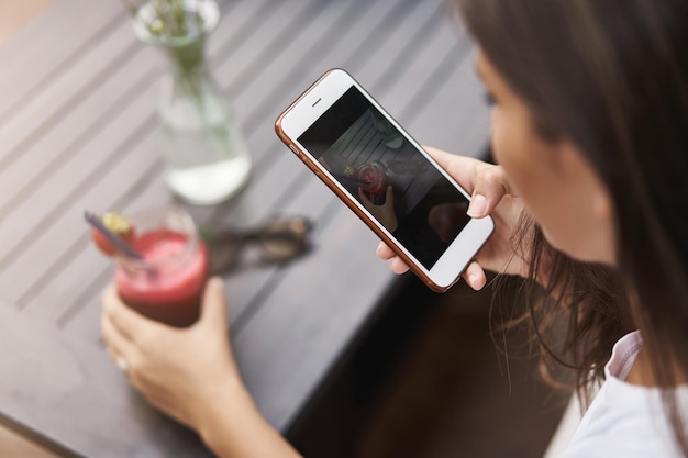 Tiro de ángulo superior joven mujer bronceada sosteniendo smartphone sit outdo