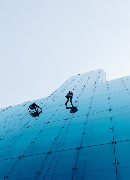 Foto gratuita tiro de ángulo bajo vertical de dos personas subiendo un edificio de cristal durante el día