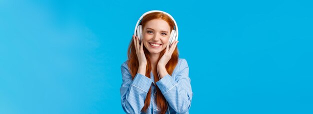 Foto gratuita tiro de cintura alegre bastante astuta chica caucásica escuchando música en auriculares grandes sonriendo complacido