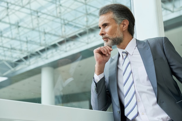 Tiro de la cintura del apuesto hombre de mediana edad con traje y corbata y reflexionando sobre nuevas ideas