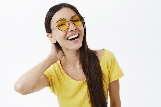 Tiro de cintura para arriba de mujer delgada joven atractiva despreocupada y feliz sociable en gafas de sol de moda y camiseta amarilla
