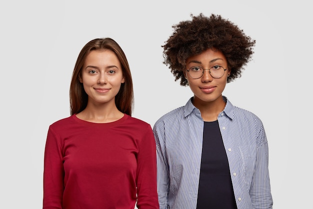 Tiro de cintura para arriba de mujeres multiétnicas de pie muy cerca una de la otra, tienen una apariencia agradable, sonríen felizmente