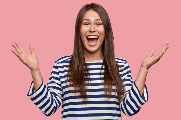 Tiro de cintura para arriba de niña feliz con piel pecosa, levanta las manos, gesticula positivamente, grita de alegría, alegre