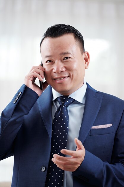 Tiro de la cintura del hombre asiático que tiene una conversación telefónica con un socio comercial