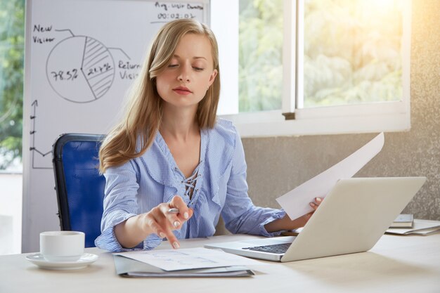 Tiro de la cintura de la joven empresaria rubia trabajando en el escritorio de la oficina