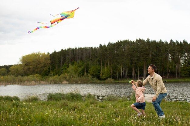 Tiro completo familia feliz volando cometa en la naturaleza