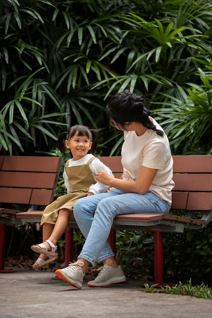 Foto gratuita tiro completo madre y niña sentada en un banco