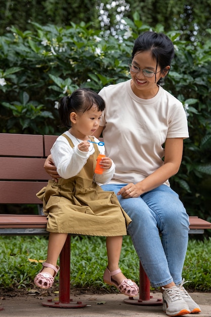 Foto gratuita tiro completo madre y niña sentada en un banco