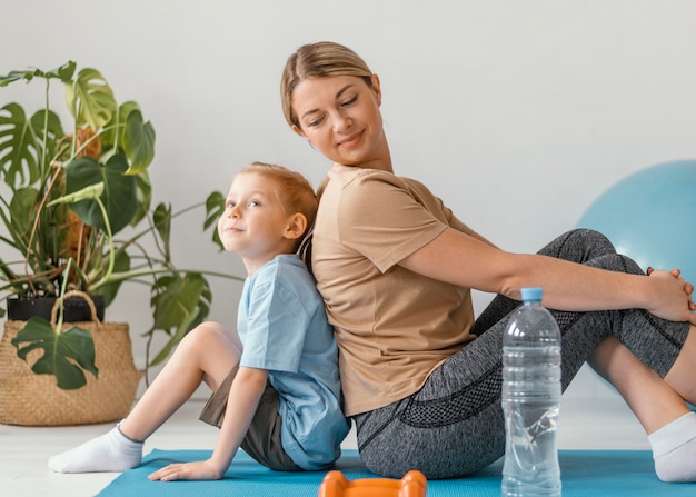 Foto gratuita tiro completo mujer y niño sentado en la estera