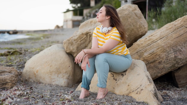 Tiro completo mujer sentada sobre las rocas en la playa