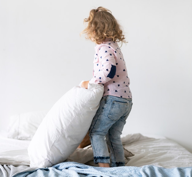 Foto gratuita tiro completo niña jugando en la cama con la almohada