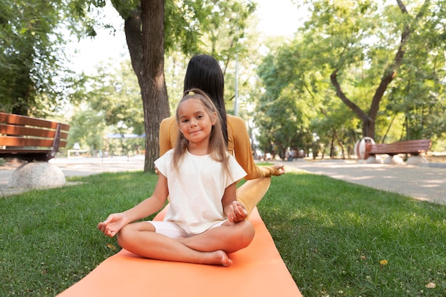 Foto gratuita tiro completo niña y mujer meditando en el parque