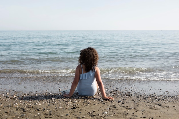 Tiro completo niña sentada en la playa