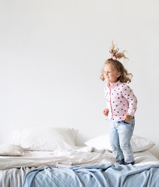 Foto gratuita tiro completo niña sonriente saltando en la cama