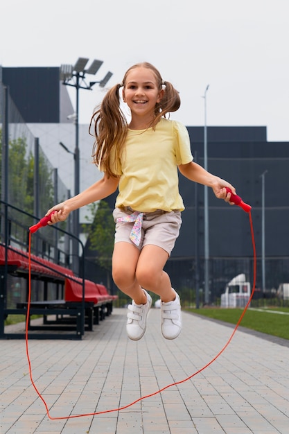 Foto gratuita tiro completo niña sonriente saltando cuerda roja