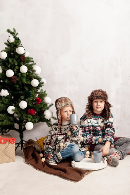Tiro completo niños sentados cerca del árbol de navidad