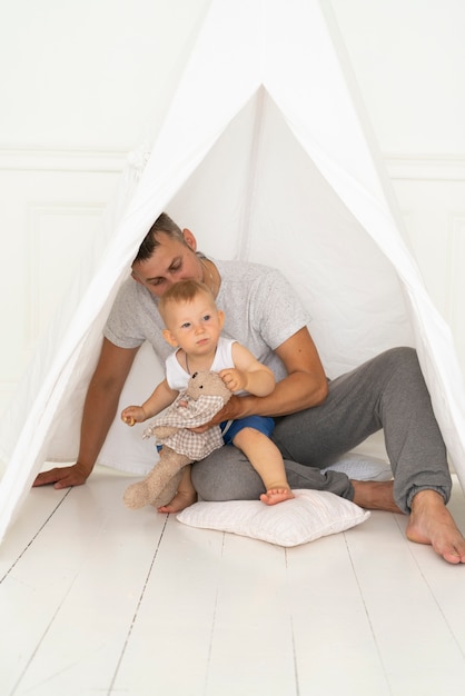 Foto gratuita tiro completo padre sentado con bebé debajo de la tienda