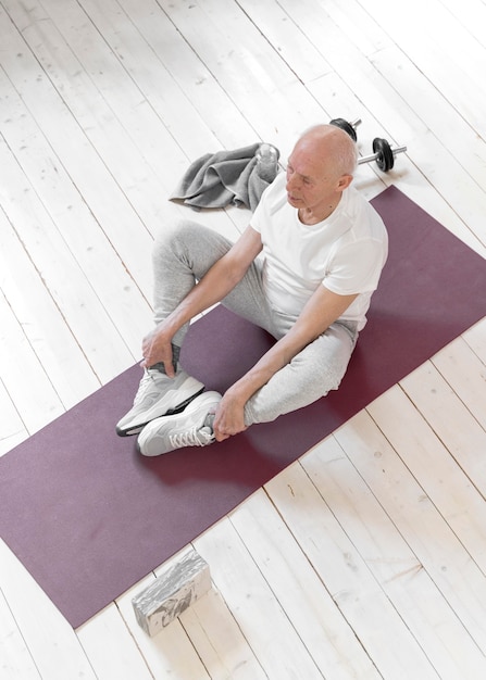 Tiro completo senior hombre sentado en la estera de yoga