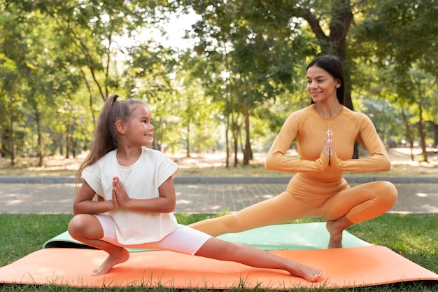 Foto gratuita tiro completo sonriente niña y mujer haciendo yoga