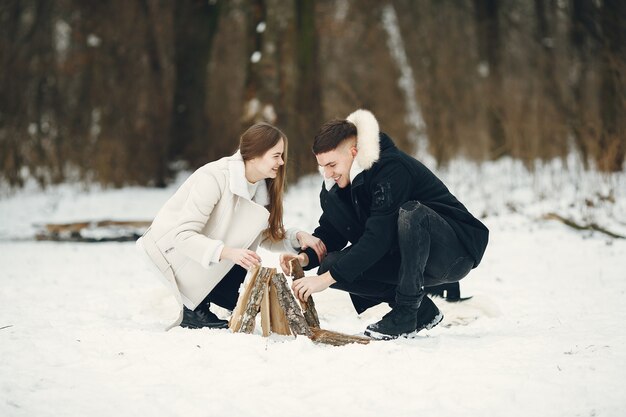 Tiro de estilo de vida de pareja en bosque nevado. Personas que pasan las vacaciones de invierno al aire libre. Gente junto a una hoguera.