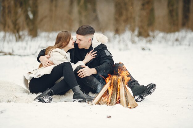 Tiro de estilo de vida de pareja en bosque nevado. Personas que pasan las vacaciones de invierno al aire libre. Gente junto a una hoguera.