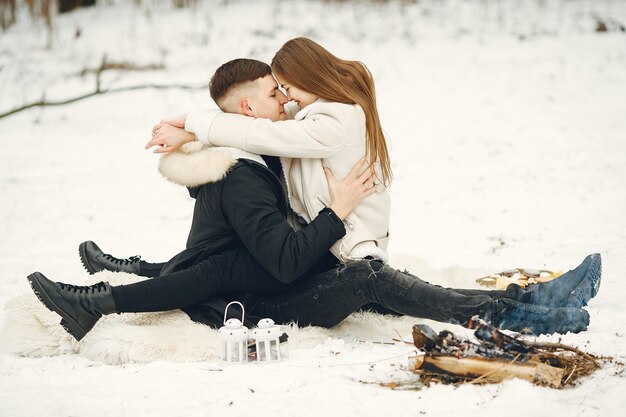 Tiro de estilo de vida de pareja en bosque nevado. Personas que pasan las vacaciones de invierno al aire libre. Gente junto a una hoguera.